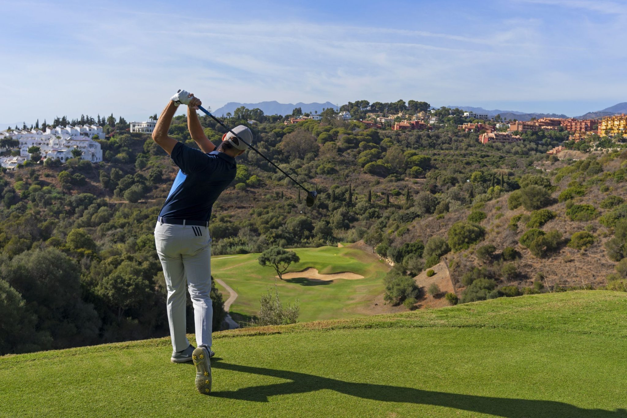 Golfer swinging with panoramic view of Cabopino Golf Course